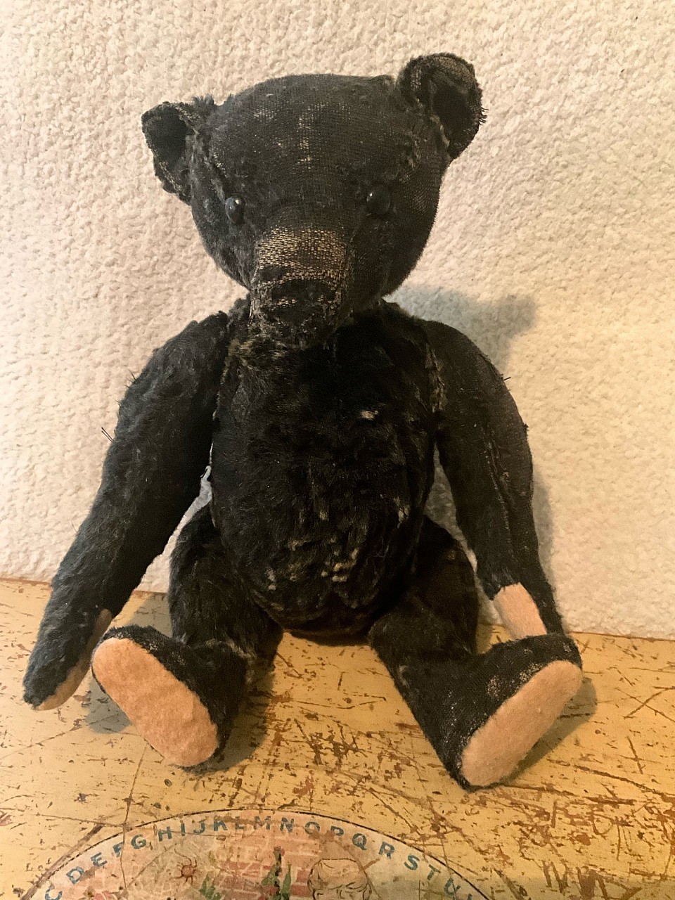 16” antique black mohair bear with boot button eyes. He feels to be stuffed with crunchy wood wool. There are areas of mohair inserts. He has a nice humpback and profile. All joints move freely and he comes wearing an antique red overall with Peek Freans teddy bear biscuit medallion pinned to it. A rare black bear indeed. ~$1495
